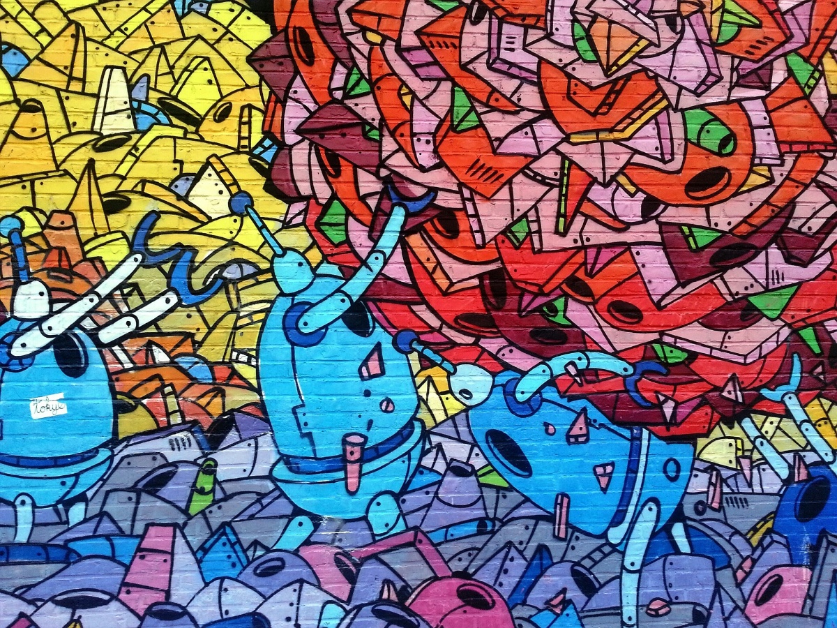 Tiiliseinään tehty graffitimaalaus, muun muassa robotin kaltaisia turkooseja hahmoja, kirkkaita värejä