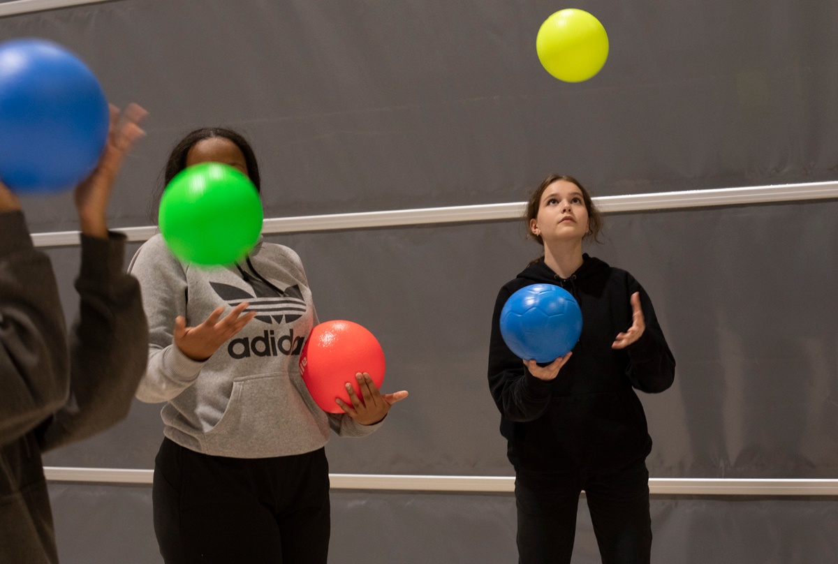 Tyttöjä heittelemässä värikkäitä palloja ilmaan.