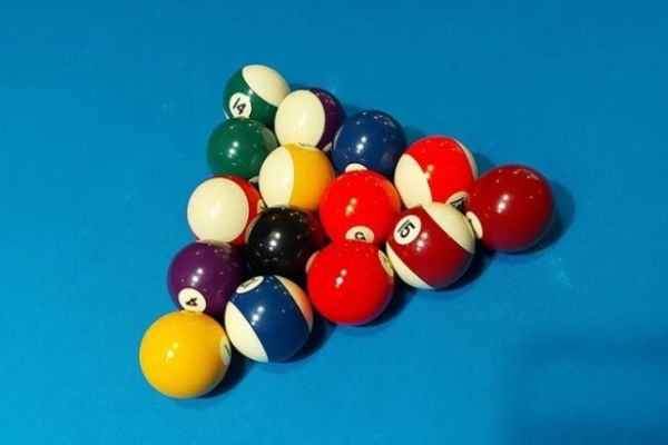 Kuvassa erivärisiä biljardipalloja kolmion muodossa valmiina peliin sinertävällä biljardipöydällä.