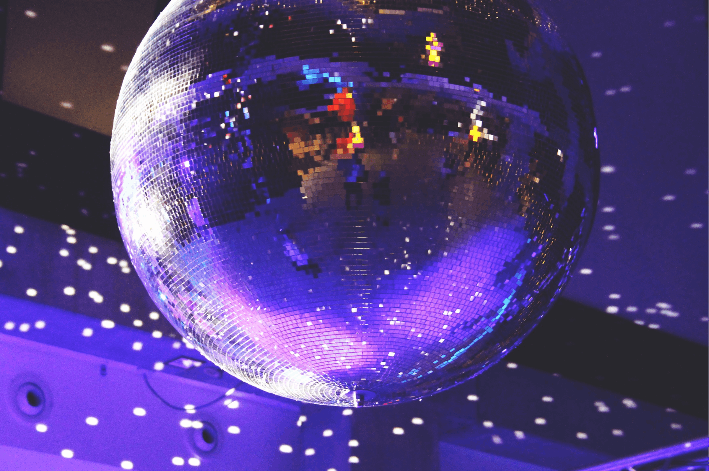 Kuvassa discopallo pyörii katossa heijastaen sinisen ja liilan sävyjä ympärilleen.