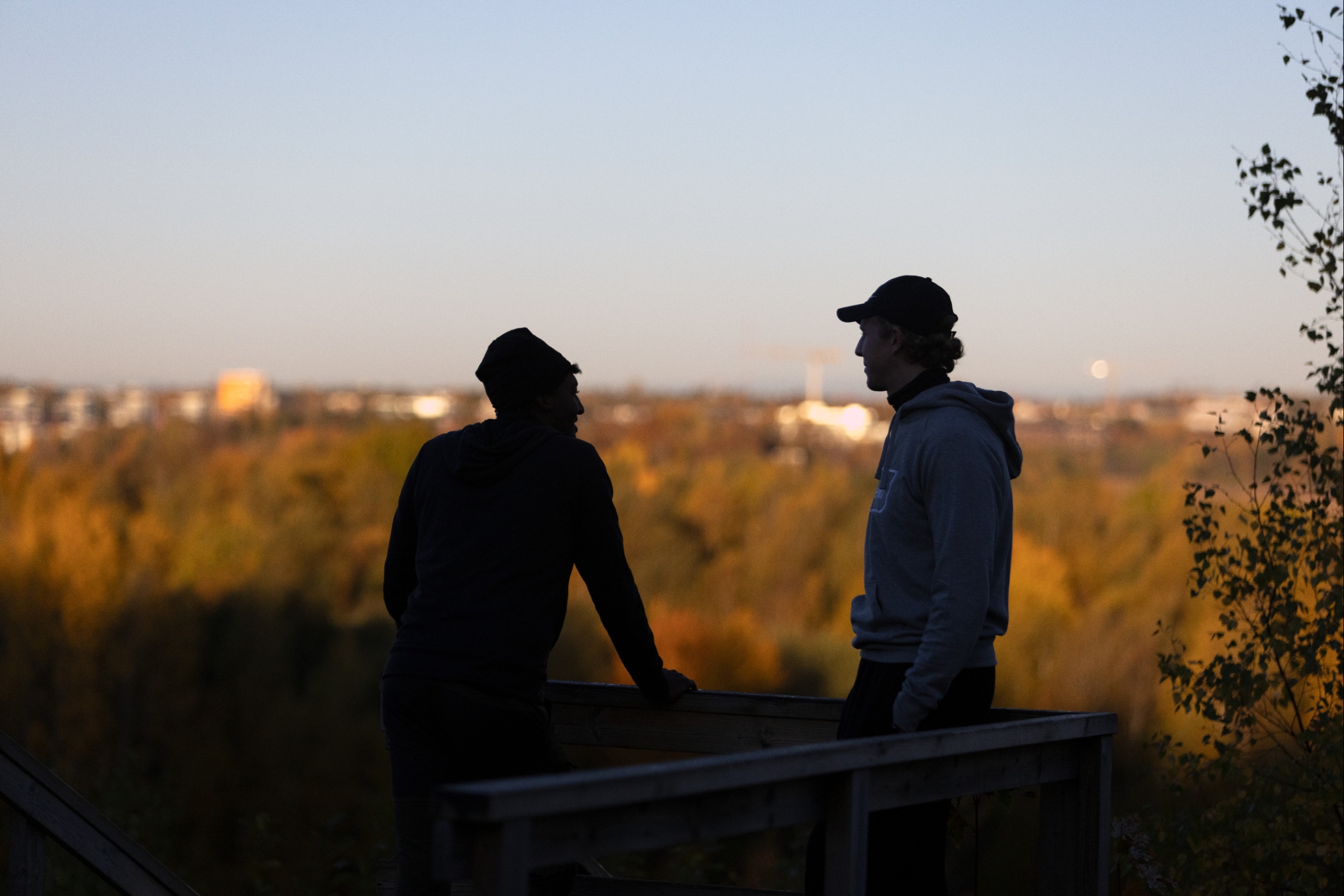 Kaksi nuorta henkilöä katsoo kaupunkia ylhäältä mäeltä.