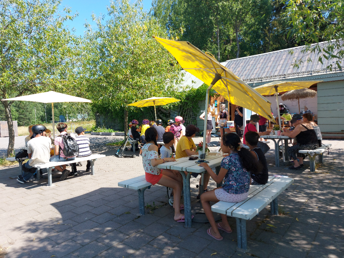 Kahvila Linnunpesän edessä lapsia nauttimassa kesäpäivästä aurinkovarjojen alla