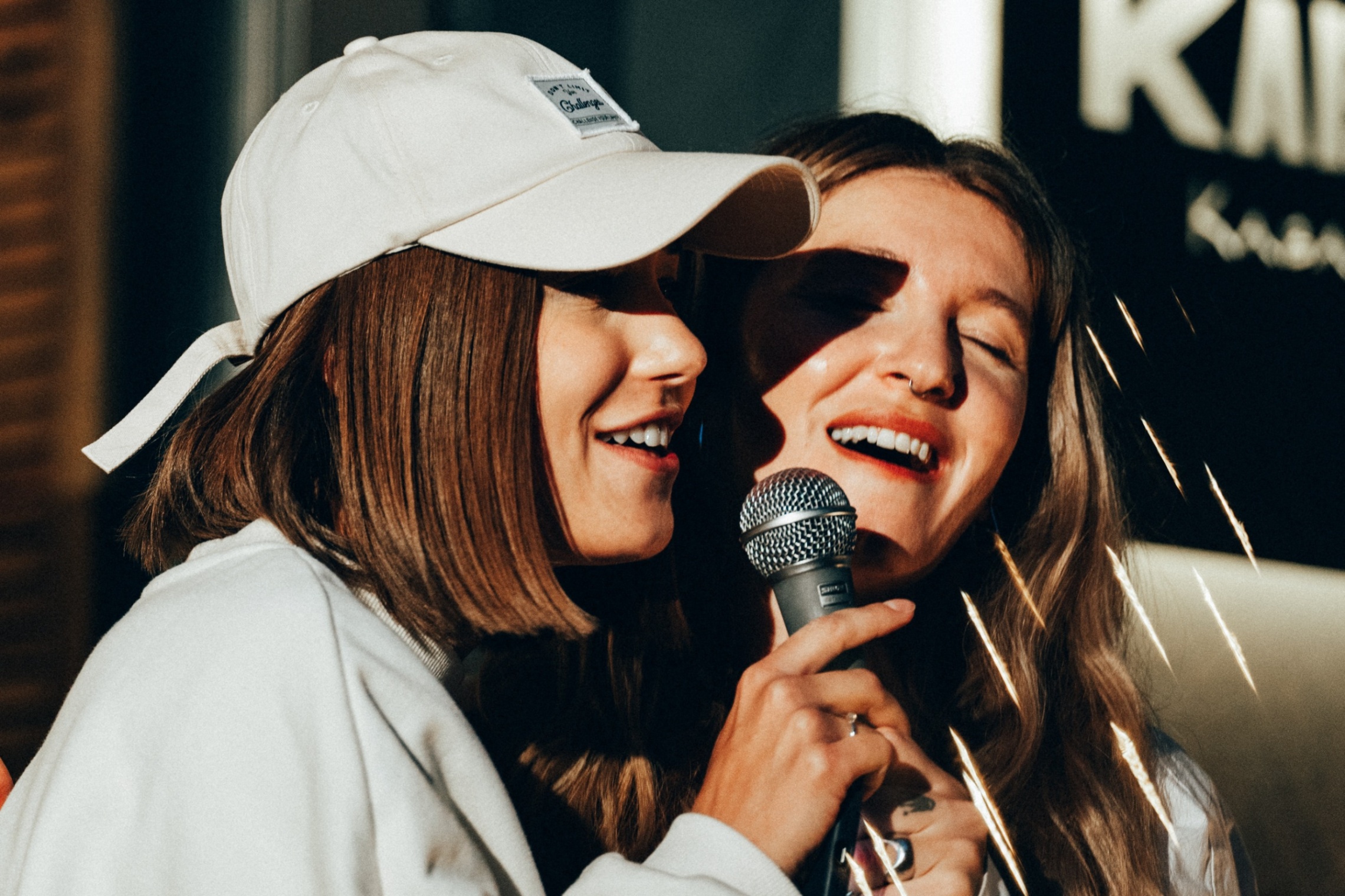 Kaksi henkilöä laulaa karaokea yhdessä hymyssä suin saman mikrofoonin äärellä.