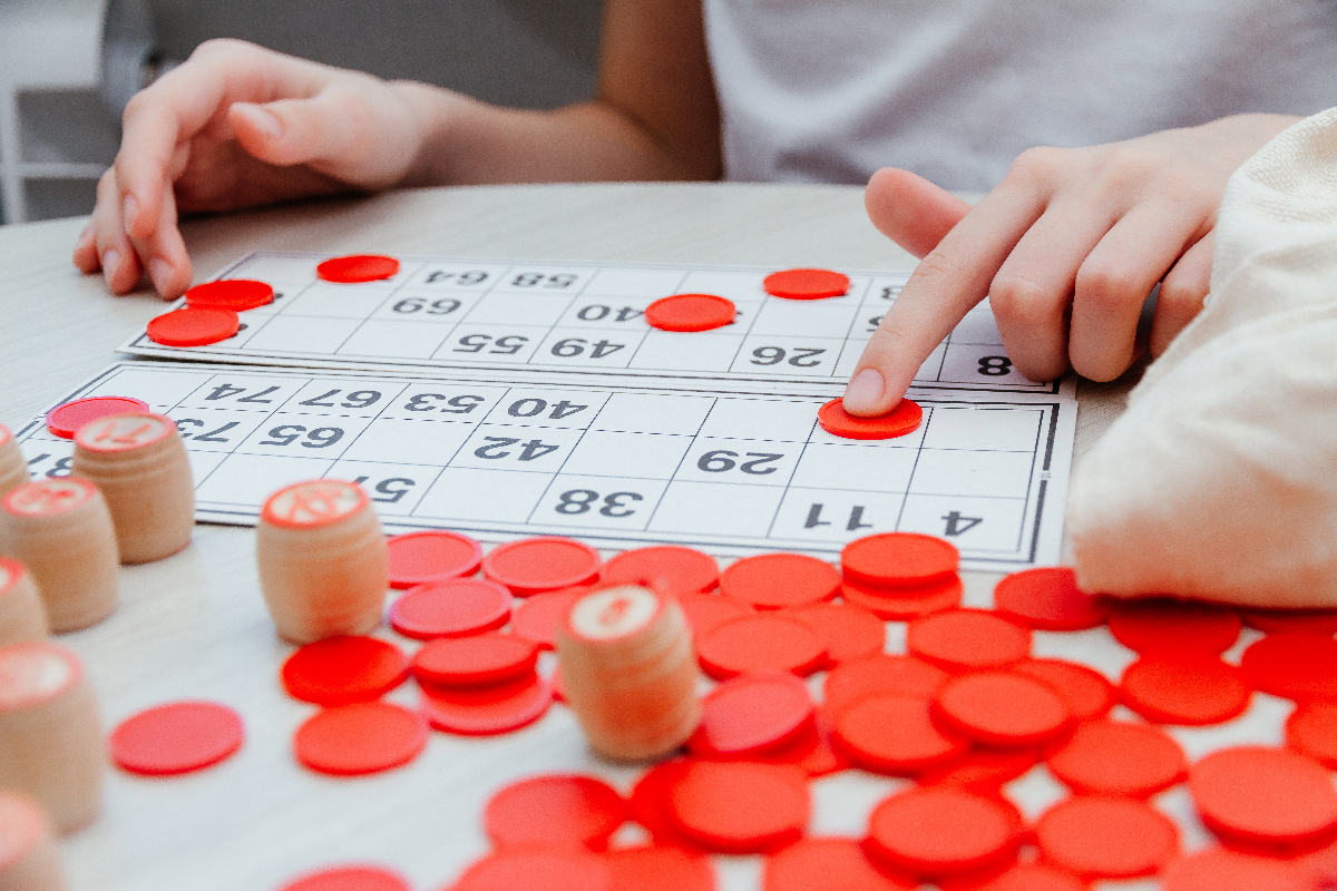 Ihminen bingopaperin ääressä, jonka vieressä punaisia pelimerkkejä.