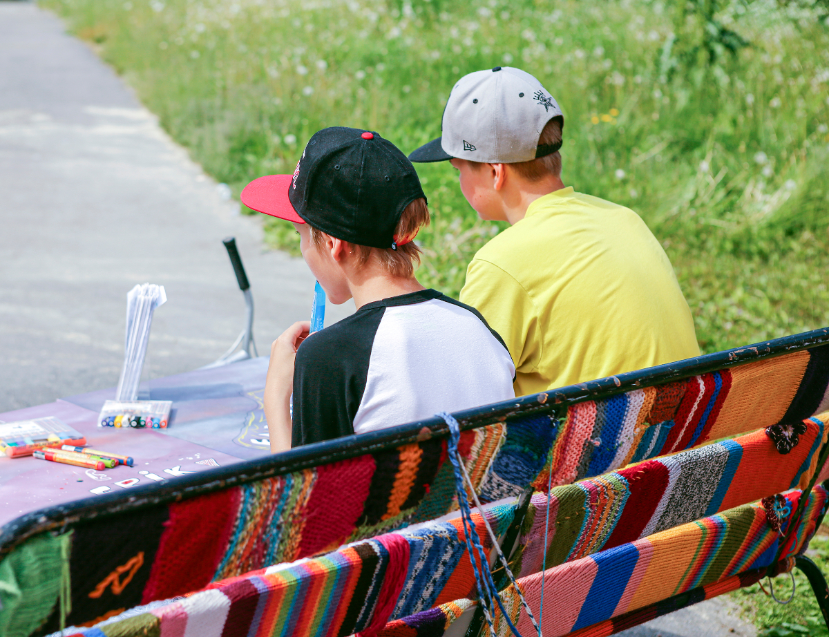 Nuoret istuvat neulegraffitilla päällystetyllä penkillä, tauolla Skuuttauksesta.