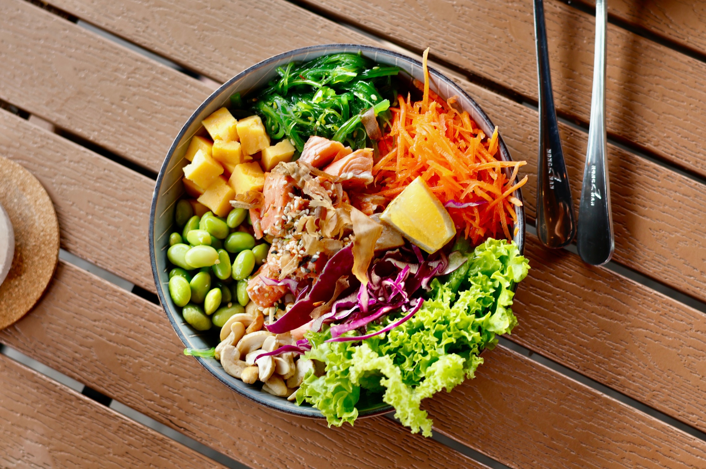 Pöydällä kulho ruokaa jossa salaattia, kasviksia, papuja ja kalaa aseteltuna kauniisti.