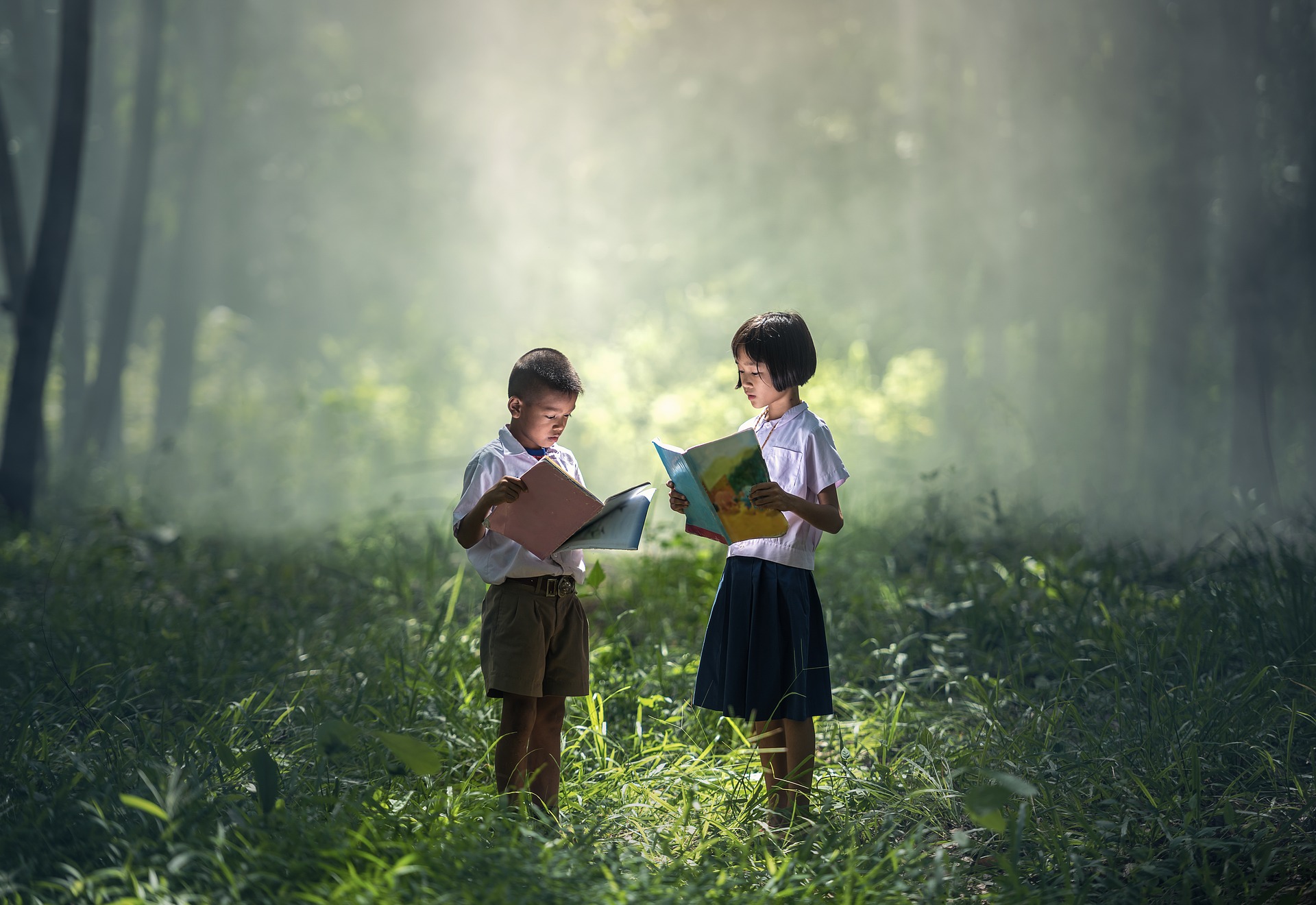 Kaksi lasta seisovat metsässä  ja lukevat kirjoja. Kuva Sasin Tipchai /Pixabay.