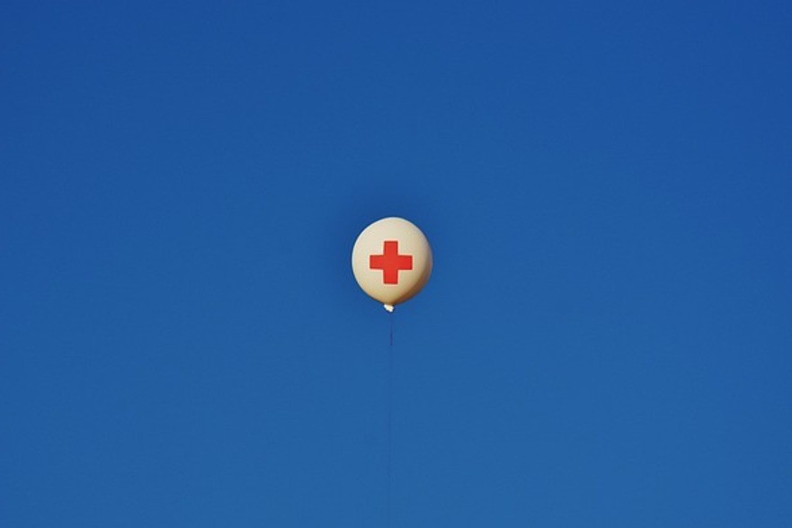 Valkoisessa ilmapallossa punainen risti sinisellä taivaalla