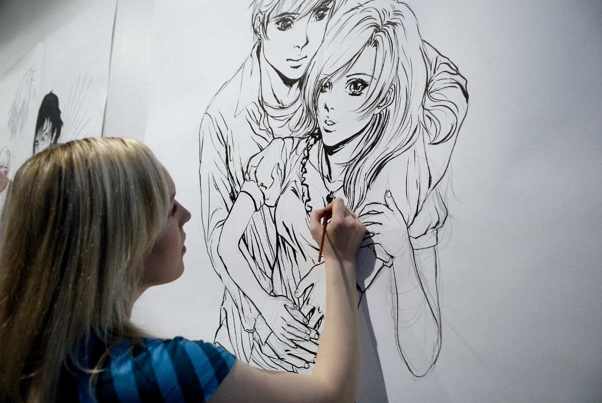 Kuvassa henkilö piirtää manga-aiheista piirustusta isolle paperille seinällä